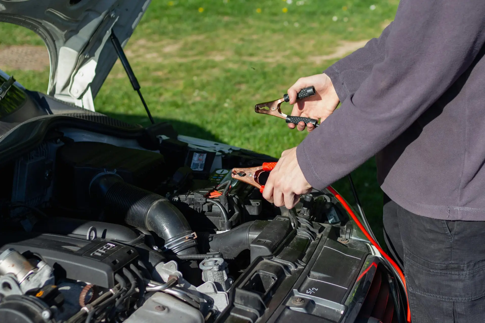 Home Close-up of mechanic using jumper cables to jump-start a car battery outdoors.